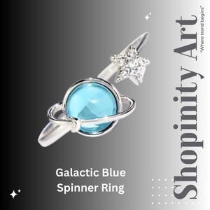 Puede incluir: Un anillo giratorio plateado con un centro en forma de planeta azul claro y un acento de estrella. El anillo presenta el texto "Galactic Blue Spinner Ring" y el logotipo de Shopinity Art.
