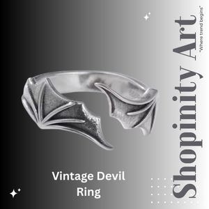 May include: A silver ring with a devil wing design. The ring has detailed wing shapes on either side, with the text "Vintage Devil Ring" below. The background has a gradient of grey and white.