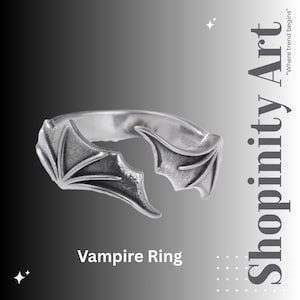 Może przedstawiać: Srebrny pierścionek z motywem skrzydła nietoperza. Pierścionek posiada dwa stylizowane skrzydła nietoperza po obu stronach, z misternymi detalami. Poniżej pierścionka widnieje napis "Vampire Ring".