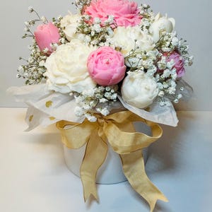 Puede incluir: Un arreglo floral con velas en forma de peon&iacute;as rosas y blancas, acentuado con delicado paniculata blanca. El ramo se presenta en una caja redonda blanca, atada con una cinta dorada. Una pieza decorativa encantadora y elegante.