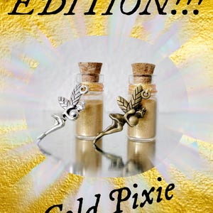 May include: Two small glass bottles filled with gold-colored powder, each sealed with a cork stopper and wrapped with gold thread. A silver-toned fairy charm and a bronze-toned fairy charm are attached to the bottles. Text reads LIMITED EDITION!!! Gold Pixie Dust!!!