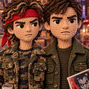 May include: Two crocheted dolls with brown hair and tan skin. The left doll wears a red headband, a camouflage jacket, and holds a comic book. The right doll wears a solid olive green jacket and holds a comic book featuring a vampire illustration.
