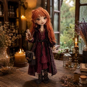 May include: A handcrafted crochet doll with long wavy ginger hair, wearing a dark burgundy dress and a matching long coat. The doll holds a small glass bottle and a black handbag, featuring detailed facial features and dark lace-up boots.