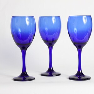 Peut inclure: Trois verres &agrave; vin bleu cobalt avec un effet d&eacute;grad&eacute;. Les verres sont vides et pos&eacute;s sur une surface blanche.