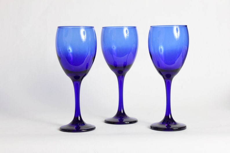 Peut inclure: Trois verres &agrave; vin bleu cobalt avec un effet d&eacute;grad&eacute;. Les verres sont vides et pos&eacute;s sur une surface blanche.