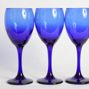 Peut inclure: Trois verres &agrave; vin bleu cobalt avec une base claire l&eacute;g&egrave;rement teint&eacute;e. Les verres sont dispos&eacute;s en rang&eacute;e, les tiges align&eacute;es.