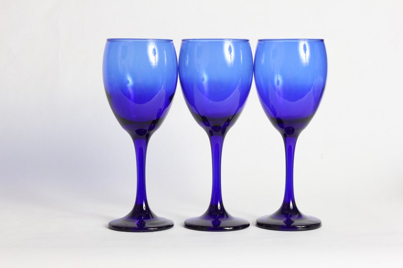Peut inclure: Trois verres &agrave; vin bleu cobalt avec un effet d&eacute;grad&eacute;. Les verres sont vides et ont un bol rond et transparent et une longue tige fine.
