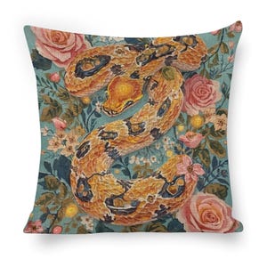 May include: A square throw pillow featuring a printed design of a coiled orange and brown snake with dark spots. The snake is surrounded by a detailed botanical pattern of pink roses, small white flowers, and green leaves on a teal blue background.