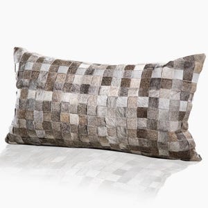 May include: Rectangular decorative pillow with a woven pattern. The pillow features a patchwork design of small, square pieces in shades of gray, brown, and cream. The pillow has a soft, textured appearance and is likely made of a natural material.
