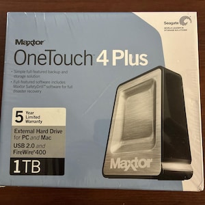 Può includere: Scatola sigillata per un disco rigido esterno Maxtor OneTouch 4 Plus. La scatola è azzurra con il nome del prodotto e le sue caratteristiche. Il disco rigido è nero e argento, con il logo Maxtor.
