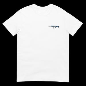 以下が含まれることがあります： 胸にAK-47ライフルを小さく描いた白いTシャツ。ライフルデザインは青とグレーの色合いを取り入れています。このTシャツは柔らかく、軽量な素材で作られています。