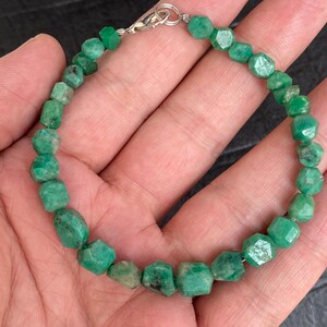 May include: A bracelet composed of faceted, irregular green gemstone beads strung together. The piece features a silver-toned metal lobster claw clasp at the top, connecting the ends of the strand of vibrant, textured, semi-precious green stones.