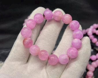 May include: A circular bracelet composed of smooth, round, translucent pink beads. The beads exhibit variations in color intensity, ranging from soft pastel pink to deeper magenta hues, and are strung together on an elastic cord to form a continuous loop.