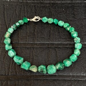 May include: A beaded bracelet featuring numerous faceted, irregular green gemstone beads strung together. The bracelet is secured with a silver-toned metal lobster claw clasp, which connects the two ends of the strand of vibrant green stones.