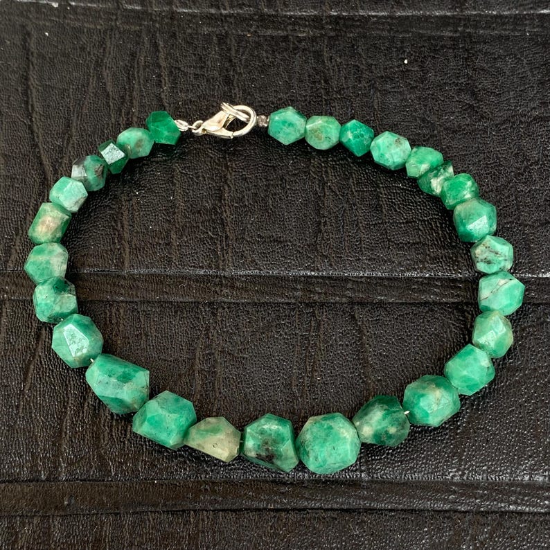 May include: A beaded bracelet featuring numerous faceted, irregular green gemstone beads strung together. The bracelet is secured with a silver-toned metal lobster claw clasp, which connects the two ends of the strand of vibrant green stones.