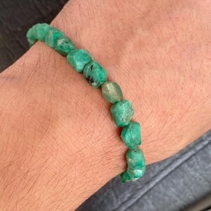 May include: A bracelet composed of faceted, irregular, raw green emerald beads strung together. The stones exhibit varying shades of deep and light green with natural inclusions and a textured, matte surface finish throughout the piece.