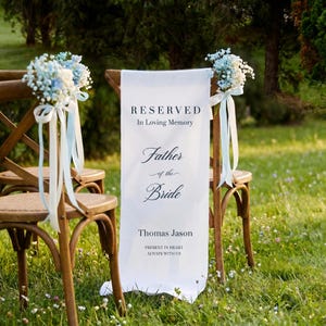 May include: Wooden chairs decorated with light blue and white floral arrangements and ribbons. A white banner on one chair reads "RESERVED In Loving Memory Father of the Bride Thomas Jason PRESENT IN HEART ALWAYS WITH US."