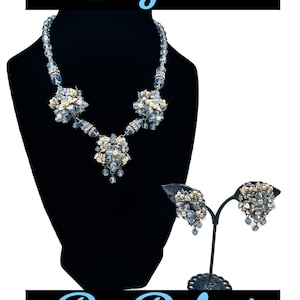 May include: A jewelry set featuring a necklace and matching earrings with blue faceted beads, cream-colored faux pearls, and clear crystals. The necklace has three floral-inspired clusters, and the earrings feature similar floral designs.