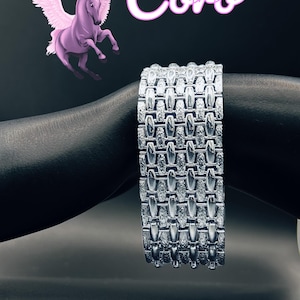 Può includere: Un bracciale in metallo color argento con un design a maglie larghe su più file, caratterizzato da segmenti rettangolari che alternano superfici lisce e testurizzate. L'immagine include un cavallo alato viola e il testo Coro in rosa.