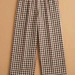 May include: Brown and white gingham print trousers with a ruffled hem. The trousers have an elasticated waistband and a wide-leg design. The fabric features a classic checkered pattern. Suitable for casual wear.