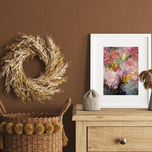 May include: A decorative arrangement featuring a wheat wreath, a framed floral print, and a woven basket with pom-poms. The artwork displays pink and yellow flowers. The basket and wreath are in shades of brown and beige, creating a warm, inviting aesthetic.