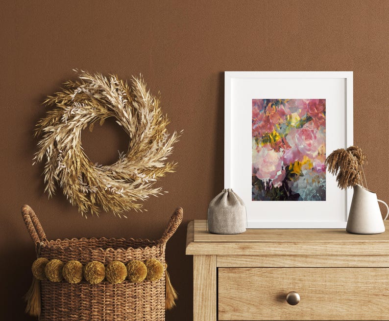 May include: A decorative arrangement featuring a wheat wreath, a framed floral print, and a woven basket with pom-poms. The artwork displays pink and yellow flowers. The basket and wreath are in shades of brown and beige, creating a warm, inviting aesthetic.