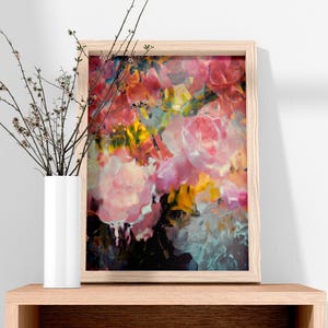 May include: A framed floral art print featuring a vibrant abstract painting with pink, yellow, and blue hues. The artwork is displayed on a wooden shelf next to a white vase with branches.