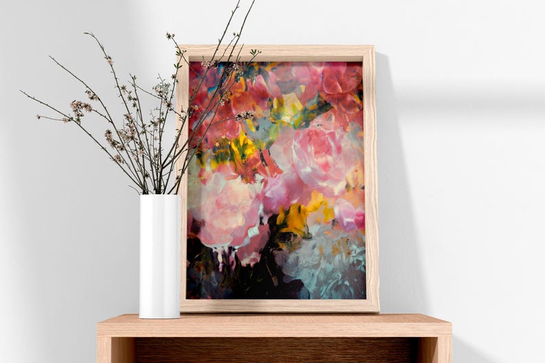 May include: A framed floral art print featuring a vibrant abstract painting with pink, yellow, and blue hues. The artwork is displayed on a wooden shelf next to a white vase with branches.