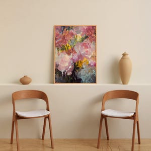 May include: An abstract floral art print in a wooden frame, featuring pink, yellow, and blue brushstrokes. Two wooden chairs with white seats are in front of a neutral wall. A vase and a decorative jar are on a shelf.