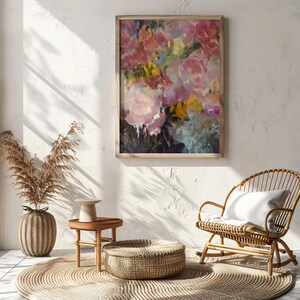 May include: A framed floral painting with pink, yellow, and blue brushstrokes hangs on a white wall. A woven rattan rocking chair with a white cushion sits nearby. A round woven rug and a small wooden table with a decorative vase complete the scene.
