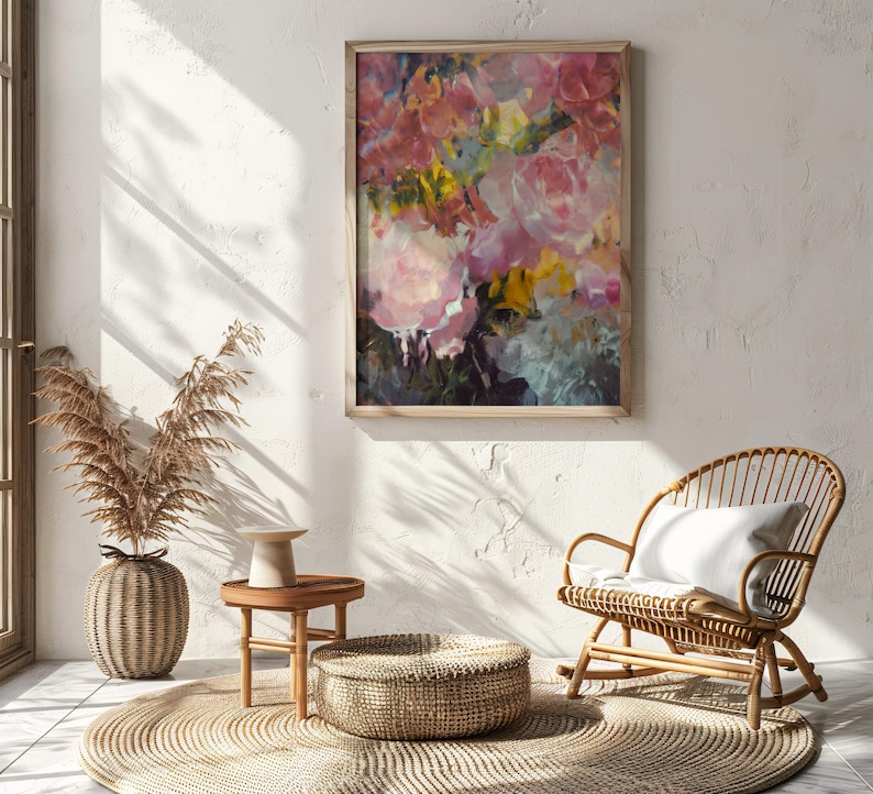May include: A framed floral painting with pink, yellow, and blue brushstrokes hangs on a white wall. A woven rattan rocking chair with a white cushion sits nearby. A round woven rug and a small wooden table with a decorative vase complete the scene.