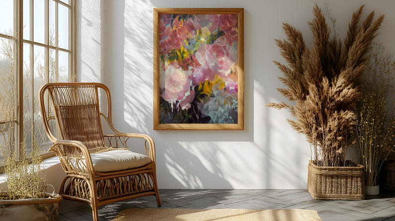 May include: A framed floral painting with pink, yellow, and white flowers hangs on a white wall. A natural wicker chair with a cream cushion sits in front of a window. Dried plants in a woven basket add to the room's decor.
