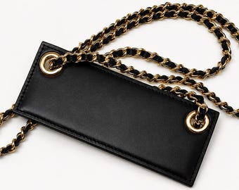 May include: A black leather bag accessory with a gold chain strap. The rectangular bag has gold eyelets for the chain to attach. The chain is gold with black leather woven through the links. The accessory is on a white background.