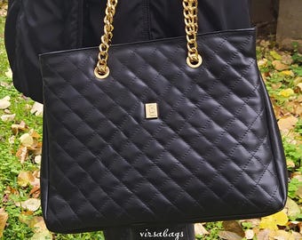 Puede incluir: Un bolso de mano negro acolchado con una correa de cadena dorada y una pequeña placa con el logotipo dorado en la parte delantera. El bolso tiene una forma rectangular estructurada con un patrón de rombos y el texto virsabags.