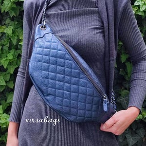May include: A navy blue quilted crossbody bag with a textured leather-like finish, a dark metal zipper closure, and a matching chain strap. The bag features a diamond-stitched pattern across the front and the text virsabags printed in white.