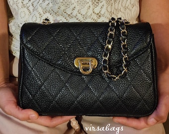 May include: Black quilted leather handbag with a gold-tone chain strap and clasp. The bag features a diamond pattern and a textured surface. The brand name "virsabags" is visible on the bottom right.