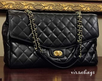May include: Black quilted leather handbag with gold-tone chain straps and hardware. The bag features a diamond pattern and a flap closure with a gold clasp. The handbag is displayed on a dark wooden surface.