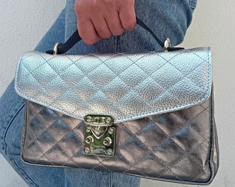 May include: A silver quilted handbag with a black strap and a gold lock. The bag has a diamond-shaped quilted pattern.