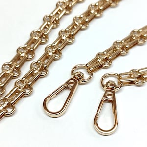 Peut inclure: Deux chaînes de sac à main dorées avec des fermoirs à mousqueton. Les chaînes sont composées de maillons ovales entrelacés.
