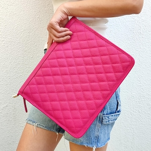 Peut inclure: Une pochette rectangulaire zippée rose vif avec un motif matelassé en losanges et une texture grainée. L'accessoire est doté d'une tirette de fermeture éclair en métal doré et d'une fermeture éclair assortie sur le bord supérieur.
