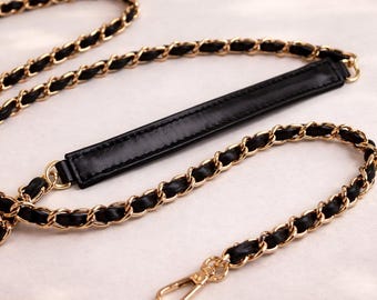 May include: A replacement handbag strap featuring a gold-tone metal chain interwoven with a black leather-like strip. The strap includes a flat, solid black shoulder pad section and a gold-tone metal lobster clasp at the end for secure attachment.