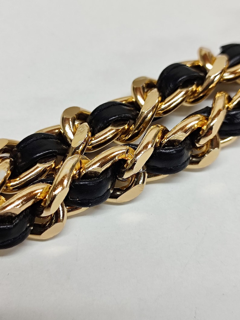 Puede incluir: Una cadena dorada con cuero negro entrelazado. La cadena es un dise&ntilde;o cl&aacute;sico con eslabones entrelazados.