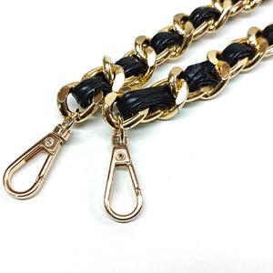 Puede incluir: Una correa de cadena de oro para bolso de mano con detalles de cuero negro y dos cierres dorados.