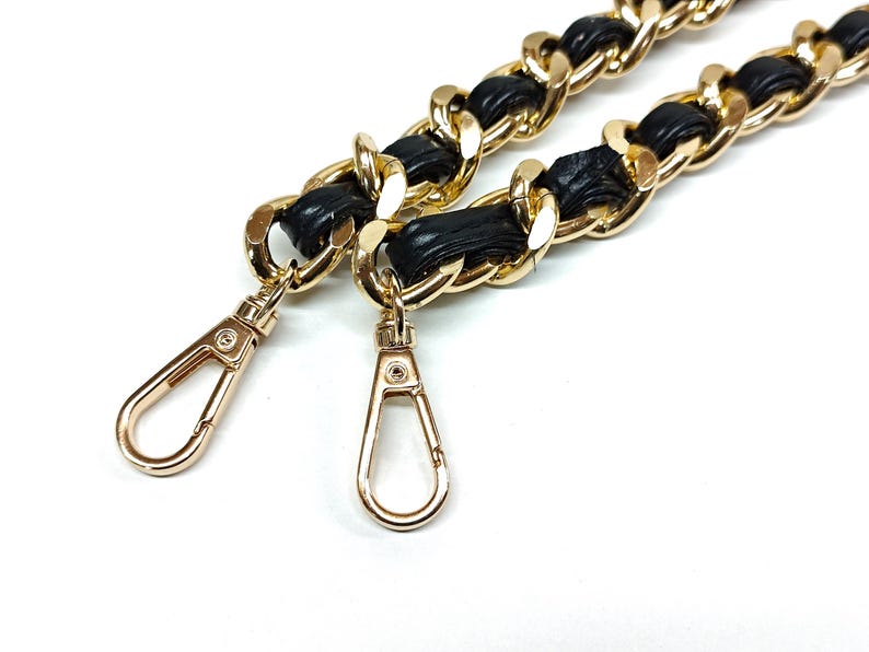 Puede incluir: Una correa de cadena de oro para bolso de mano con detalles de cuero negro y dos cierres dorados.