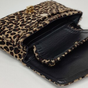 May include: A rectangular shoulder bag featuring a textured leopard print pattern in shades of brown and black. The bag has a gold-toned metal clasp closure on the front flap and a black interior lining with a gold chain strap attachment.