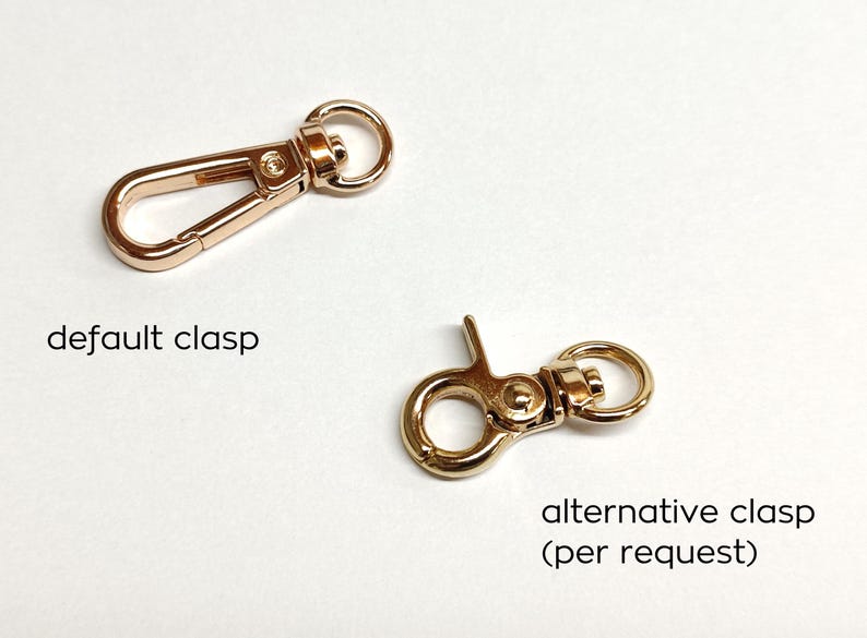 May include: Two gold-toned metal clasps for bags or purses. The clasp on the left is a traditional hook and loop style. The clasp on the right is a more modern, circular style. The text "default clasp" is below the left clasp and the text "alternative clasp (per request)" is below the right clasp.