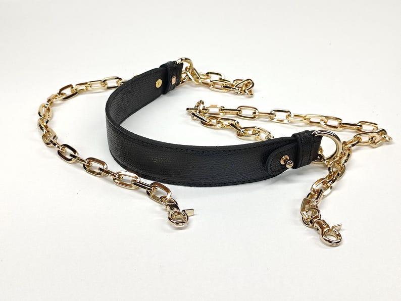 May include: Black leather handbag strap with gold-colored chain links and hardware. The strap has a curved, padded section for the shoulder and gold-tone clasps for attachment. The chain links are a medium size.