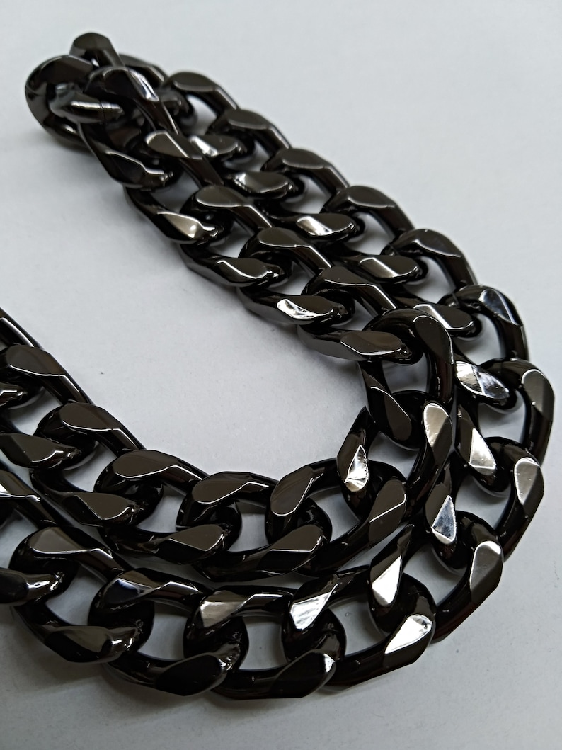 Peut inclure: Un collier cha&icirc;ne &eacute;pais noir avec un design &agrave; maillons plats. La cha&icirc;ne est en m&eacute;tal et a une finition brillante.