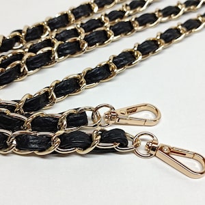 May include: A black and gold chain strap with two gold clasps. The chain is made of interwoven leather and metal links.