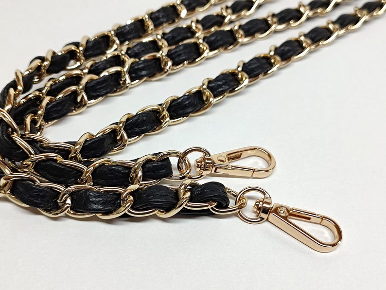 May include: A black and gold chain strap with two gold clasps. The chain is made of interwoven leather and metal links.